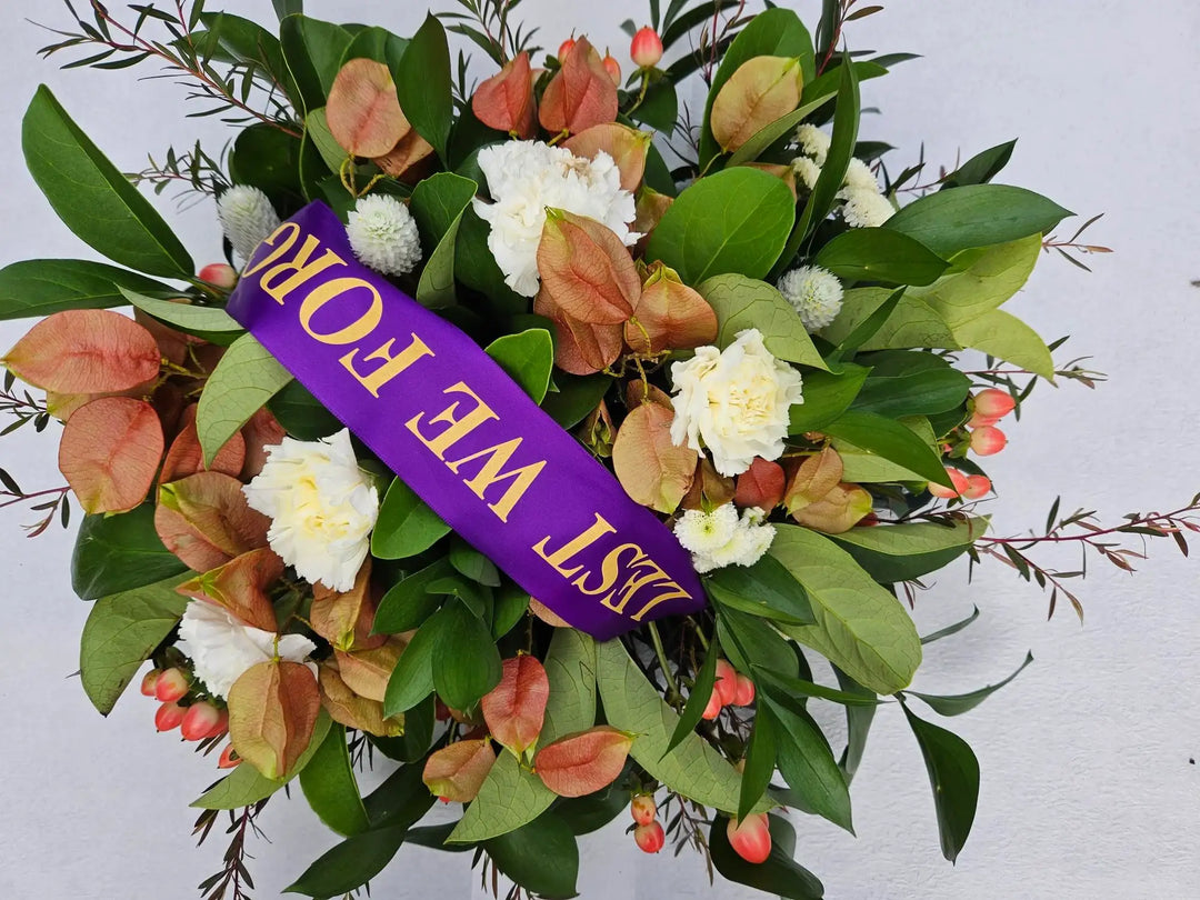 White carnations, dried paper daisies, and green foliage in a sympathy wreath with purple &