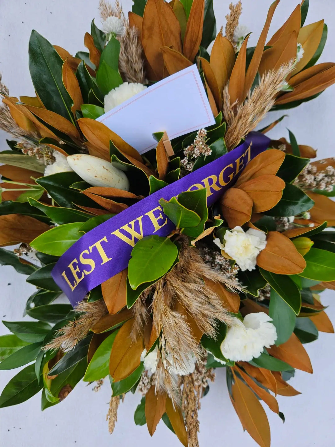 Lest We Forget wreath with magnolia leaves, white blooms, and dried grasses for remembrance