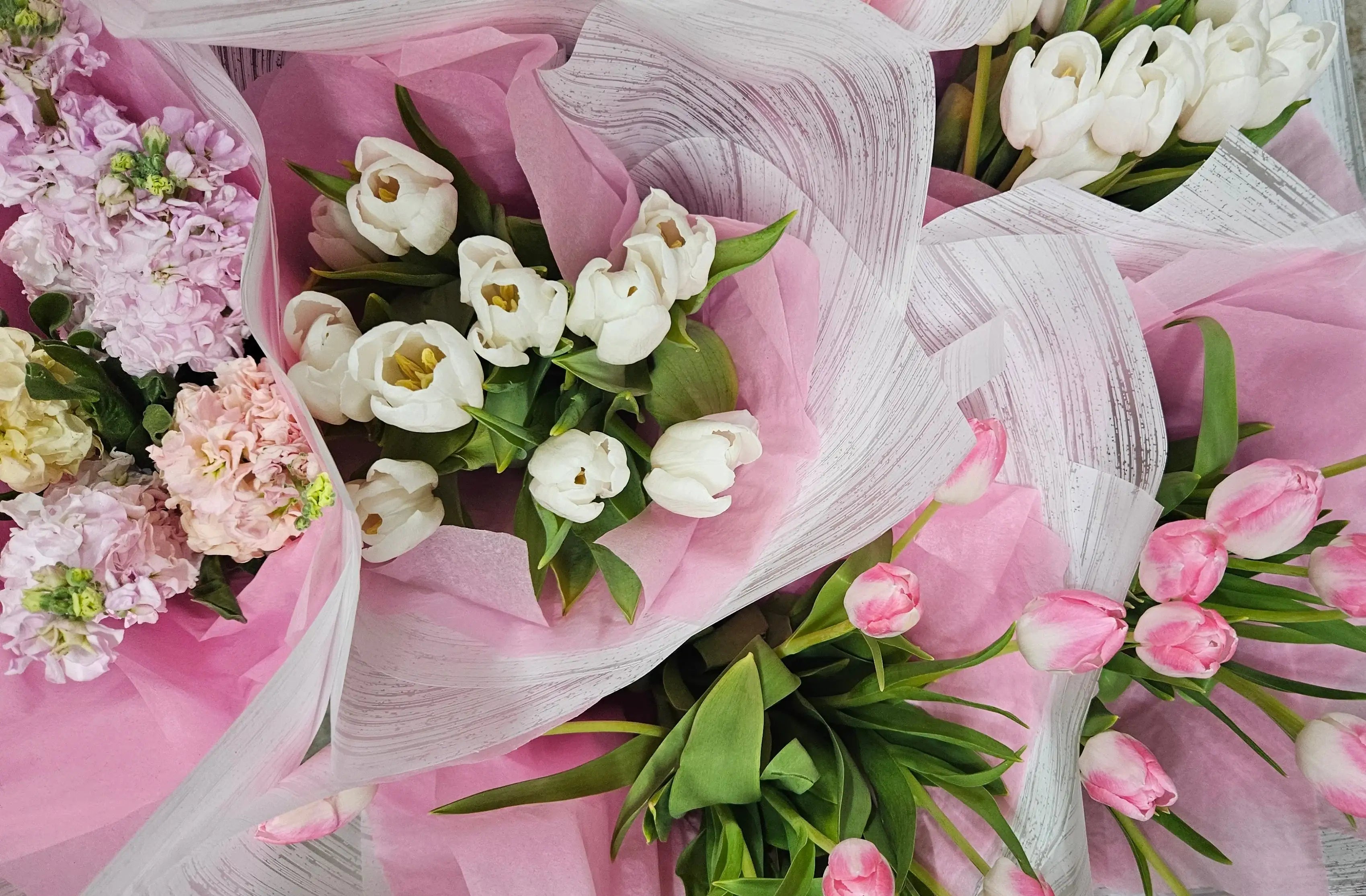 Bouquets of pink and white flowers wrapped in paper on a surface.