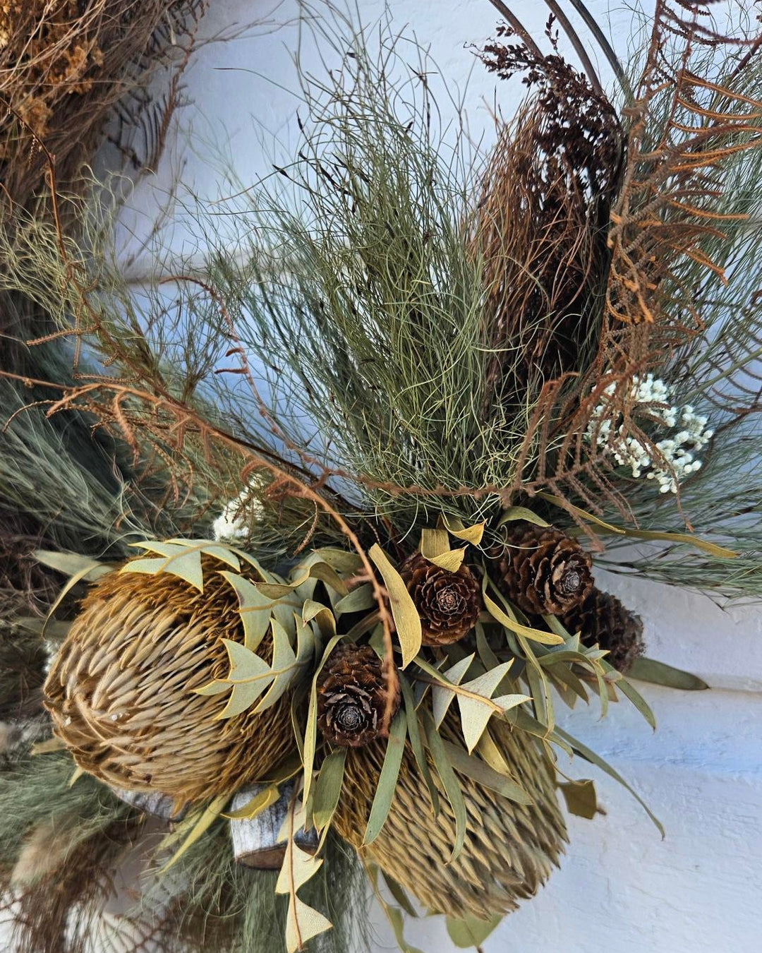 Decorative wreath with greenery, pinecones, and twine on a white background