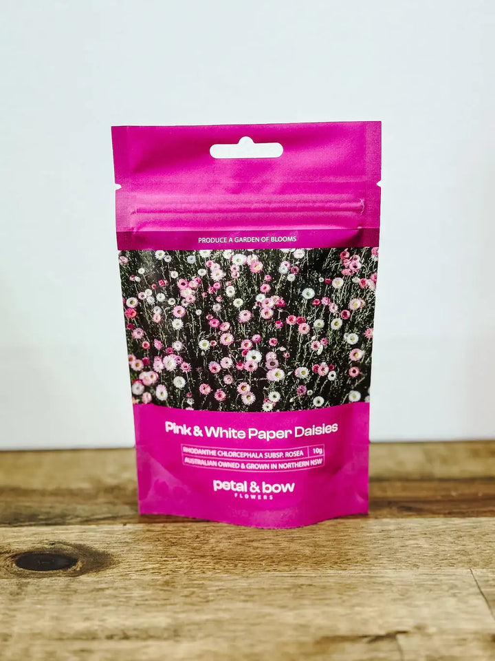 Packaging of Petal and Bow flowers pink and white everlasting paper daisiy seed packet on a wooden surface with a white background