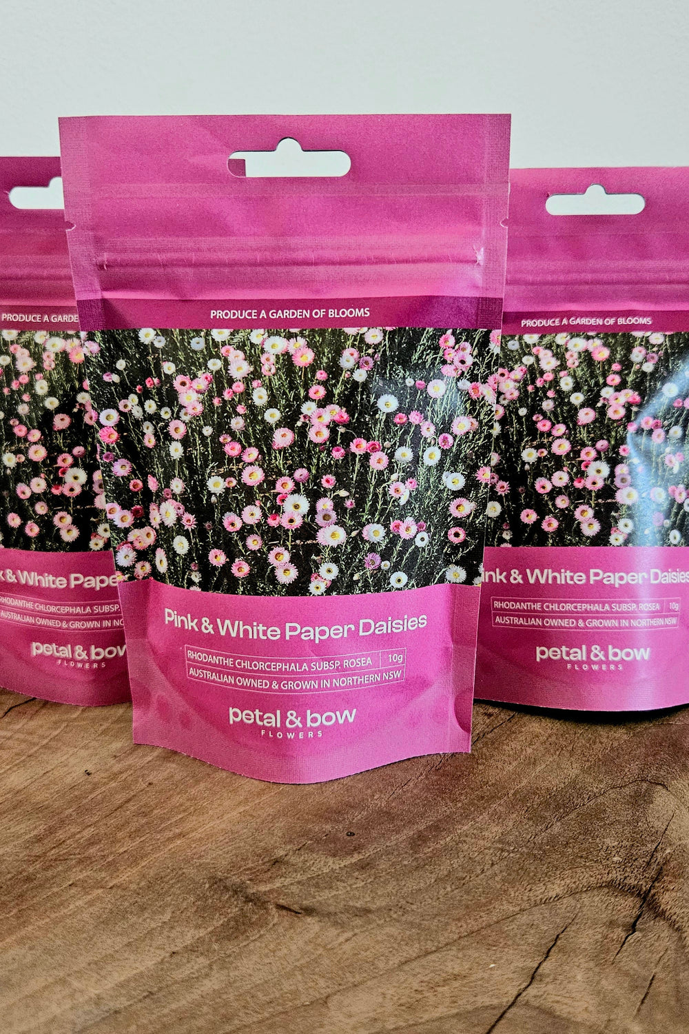 Three packages of pink and white paper daisies on a wooden surface with a white background