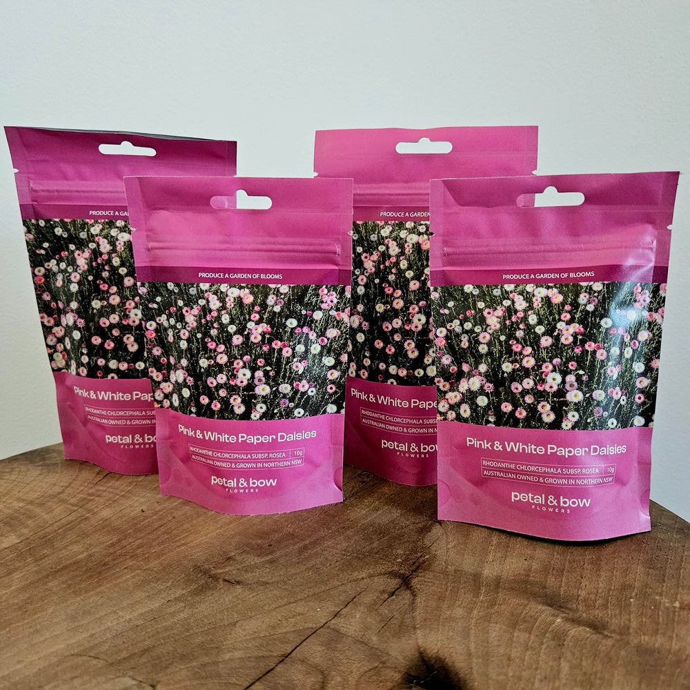 Five packages of Petal and Bow flowers pink and white paper daisies on a wooden shop shelf