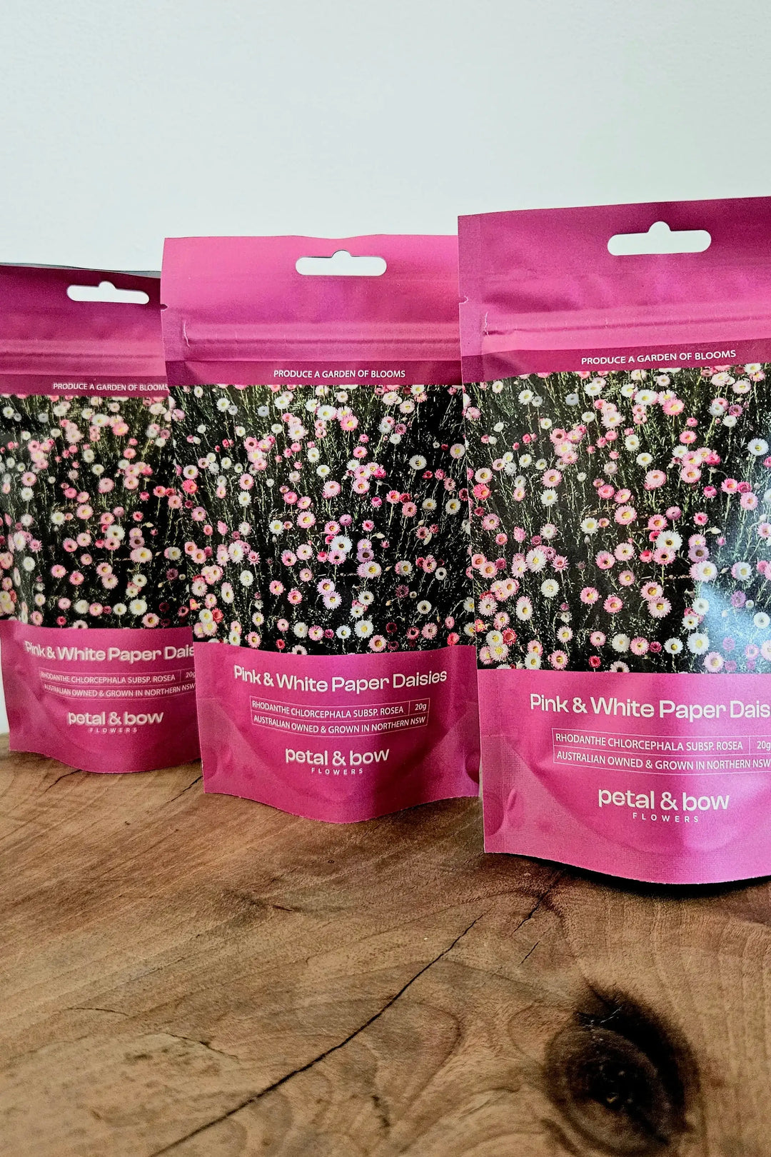 Three packages of Petal and Bow Paper Daisy seed packets on a wooden shelf with a white background.