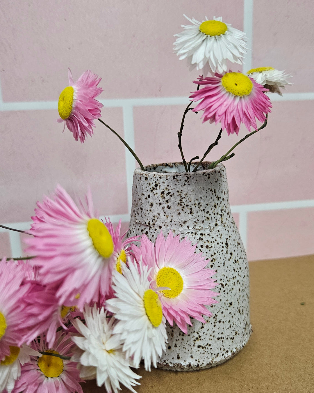 Decorative ceramic vase with pink and white dried paper daisy flowers. 