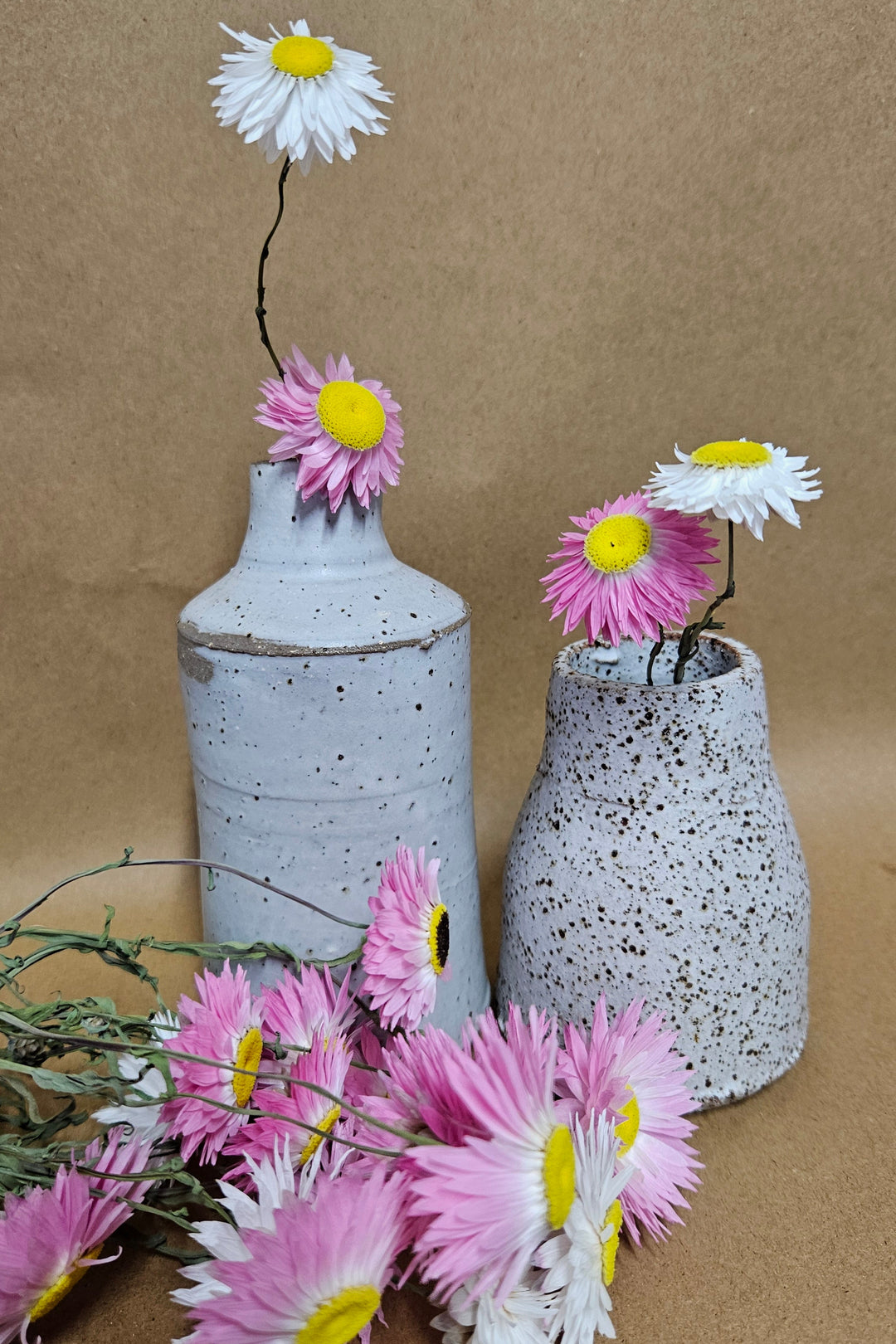 Two ceramic vases filled with pink and white dried paper daisies. 