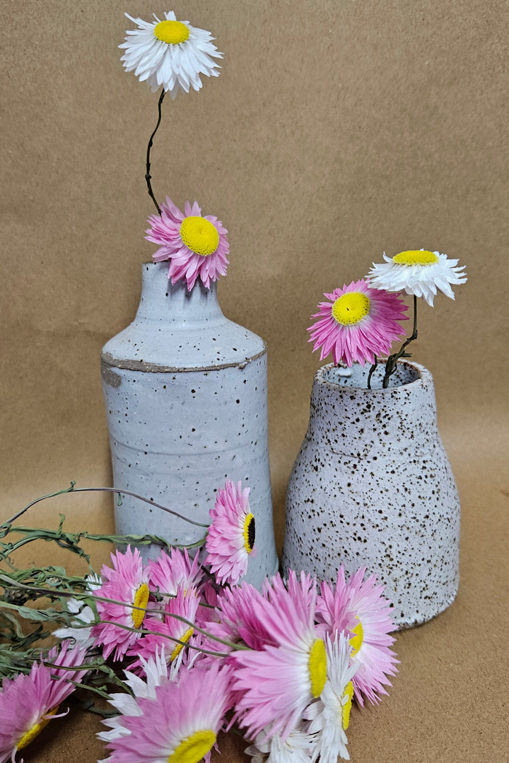 Two ceramic vases filled with pink and white dried paper daisies. 